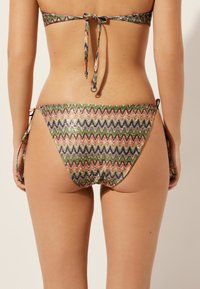Majtki bikini z wielokolorowym wzorem w zygzaki, z błyszczącą teksturą i regulowanymi wiązaniami po bokach, które zapewniają możliwość dopasowania.