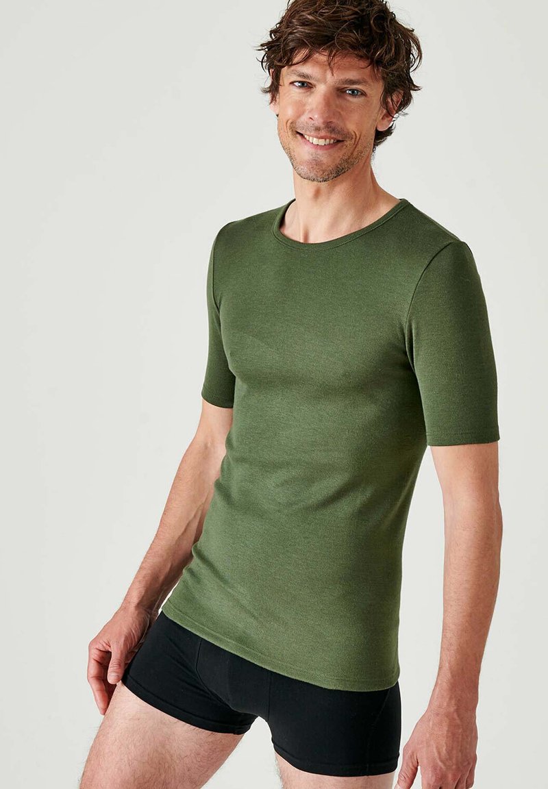 T-shirt verde a maniche corte in cotone morbido, con collo rotondo e vestibilità slim, abbinato a pantaloni corti neri aderenti.