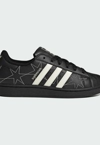Black leather sneakers with white star and three-stripe design. Features a textured rubber toe cap and padded collar for comfort.