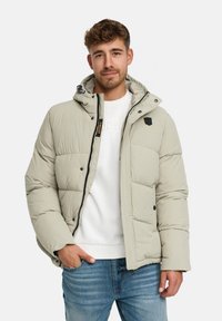 Puchowa, jasnoszara kurtka z odpinanym kapturem, z zamkiem błyskawicznym i bocznymi kieszeniami. Noszona na białym swetrze i niebieskich dżinsach.