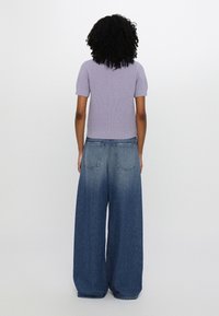 Top corto a maniche corte lilla a coste abbinato a jeans in denim blu a gamba larga. I jeans presentano tasche posteriori e un leggero effetto ombre all'orlo.