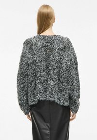 Suéter de punto gris y negro con un patrón de cable texturizado, corte holgado y dobladillo recortado. La parte posterior presenta un escote redondo y tejido suave.