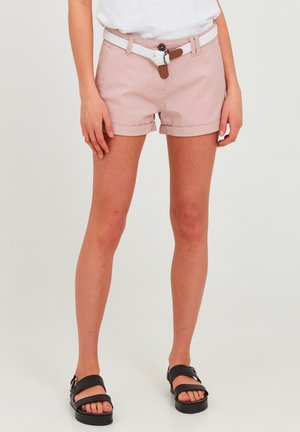 Lyserøde denimshorts med opsmøget kant, udstyret med et hvidt fletbælte og brune læderdetaljer. Båret med sorte sandaler med remme.