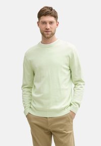 Lichtgroene crewneck sweater van zacht materiaal, met ribgebreide manchetten en zoom, tentoongesteld op een neutrale achtergrond met beige broeken.