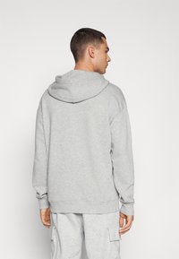 Hoodie gris en tissu doux, avec une capuche à cordon et des poignets côtelés. Design uni avec une coupe décontractée, vu de dos.