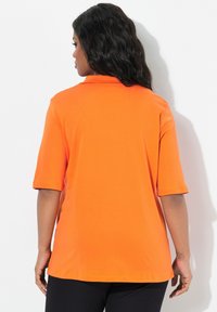 Oranje poloshirt met korte mouwen, een zachte textuur en een relaxte pasvorm. Heeft een klassieke kraag en zijsplitten aan de zoom.