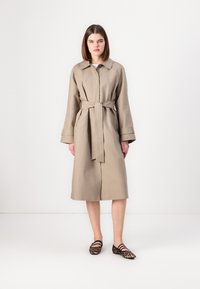 Beige-Trenchcoat mit tailliertem Gürtel, Kragen und langen Ärmeln. Strukturierter Stoff und Seiten Taschen. Kombiniert mit Ballerinas im Leopardenmuster.
