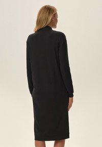 Czarna sukienka z długim rękawem o prostym kroju, sięgająca do połowy łydki. Miękka tkanina, minimalistyczny design i brak widocznych wzorów lub akcentów.