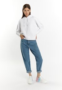 Vit sweatshirt med huva, avslappnad passform, med snörning. Ljusblå denimjeans, smalning nedtill, uppvikta vid anklarna. Vita sneakers med gradientaccenter.