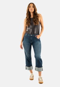 Top sin mangas de color gris oscuro combinado con jeans cortos de color azul medio con dobladillos vueltos, complementado con zapatillas beige con acentos claros.