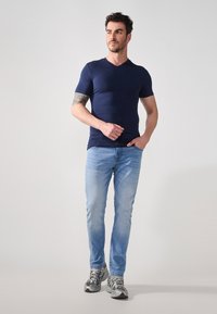 Marineblå kortermet V-hals T-skjorte, kombinert med lyseblå jeans og grå joggesko. Glatt tekstur, tettsittende design, uformell stil.