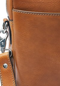 Tan leather bag close-up showing detailed stitching and a silver metal clasp attached to a detachable strap.