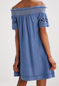 Jeanskleid mit schulterfreiem Schnitt, kurzen bestickten Ärmeln, einem gerafften Oberteil und einem ausgestellten Saum in mittelblauer Farbe.