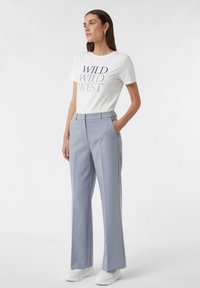 Biała koszulka z czarnym napisem "WILD WILD WEST", w połączeniu z jasnoszarymi spodniami o szerokich nogawkach i białymi sneakersami. Gładki materiał i dopasowany krój.