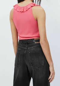 Różowa prążkowana bluzka bez rękawów z falbaniastym dekoltem, w połączeniu z wysokim stanem czarnych dżinsów z tylnymi kieszeniami i dopasowaną talią.