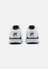 Fehér Nike sportcipők fekete részletekkel, sima felsőrésszel, párnázott bokarésszel és gumitalppal. A márkázás a saroknál látható.