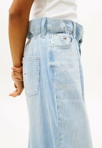 Falda de mezclilla de rayas azul claro con una cinturilla fruncida, bolsillos laterales y un parche con el logo en el bolsillo trasero, mostrando un acabado texturizado.