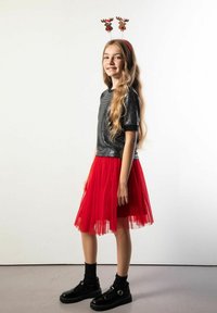 Czarna bluzka z cekinami, czerwona spódnica z tiulu, czarne botki z klamrami oraz opaska na głowę z porożem renifera. Długie falowane włosy i neutralne tło.