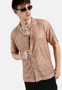 Camicia a maniche corte, di colore rosa con motivo a fantasia e ritagli a forma di diamante, dotata di chiusura con bottoni, vestibilità rilassata e dettagli in nero.