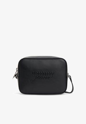 Czarna, prostokątna torba na ramię z wytłoczonym logo "tommy jeans" z przodu i regulowanym paskiem na jednolitym białym tle.