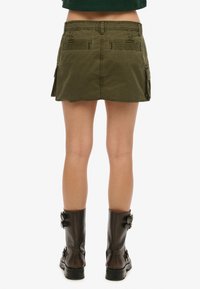 Cargo rok in olijfgroen met een rechte snit, twee achterzakken en een gerafelde zoom. Gecombineerd met zwarte laarzen tot de knie.