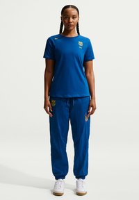 Blå atletisk t-shirt med rund hals och korta ärmar, matchad med blå joggingbyxor med logotyp och elastiska muddar, mot en neutral bakgrund.