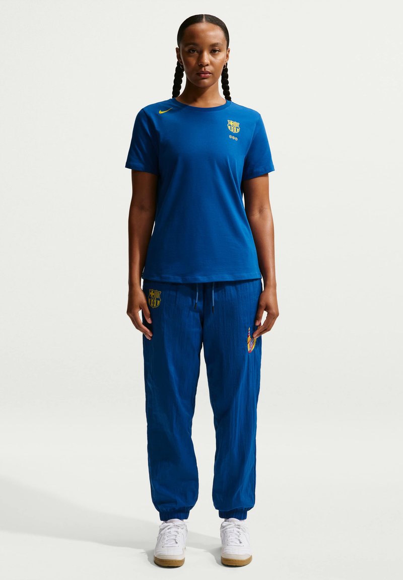 Blå atletisk t-shirt med rund hals och korta ärmar, matchad med blå joggingbyxor med logotyp och elastiska muddar, mot en neutral bakgrund.