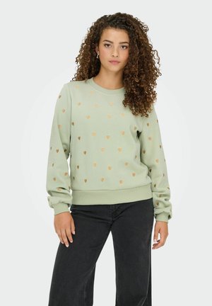 Sweatshirt vert menthe avec des motifs de cœurs dorés, col et poignets côtelés, et coupe décontractée. Assorti avec un pantalon noir à jambes larges.