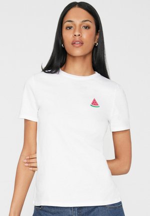 Frau mit langen schwarzen Haaren, die ein weißes kurzärmeliges Hemd mit einer kleinen Stickerei einer Wassermelone auf der Brust trägt.