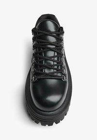 Čierna kožená turistická obuv s hrubou podrážkou, kovovými očkami a čiernymi šnúrkami viazanými do krížového vzoru, zobrazená zhora.