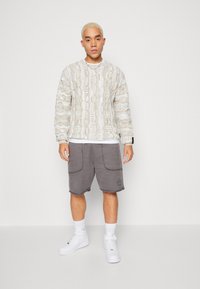 Light-colored patterned sweatshirt with textured design, paired with gray shorts featuring pockets. Worn with white sneakers and socks.