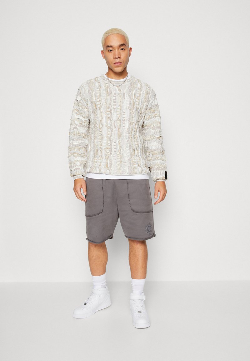 Light-colored patterned sweatshirt with textured design, paired with gray shorts featuring pockets. Worn with white sneakers and socks.