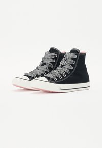 Sapatilhas altas de lona pretas com atacadores em padrão xadrez preto e branco, solas de borracha brancas e detalhes em rosa no interior e na sola.