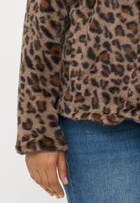 Jachetă din blană sintetică cu imprimeu leopardo, având o textură moale, cu mâneci lungi și o margine ușor scurtă. Pur tată cu pantaloni din denim albastru.
