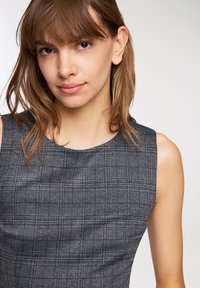 Szara w kratę sukienka bez rękawów z okrągłym dekoltem, wykonana z teksturowanej tkaniny z subtelnym wzorem w kratkę, podkreślająca detale krawieckie.