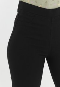 Leggings neri a vita alta, realizzati in tessuto elastico, caratterizzati da una texture liscia, senza chiusure visibili e con un design semplice.