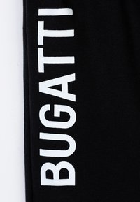 Pantaloni felpati neri con un audace logo "BUGATTI" bianco stampato verticalmente lungo la gamba sinistra. Tessuto morbido e elastico con una superficie liscia.