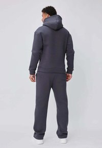 Ensemble sweat à capuche et pantalon de survêtement gris, fabriqué en tissu doux, doté d'une capuche, de poches latérales et de poignets côtelés, avec une coupe décontractée et un design minimaliste.