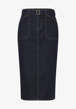 Kvinde iført mørk denimsnørk med forlommer og bæltedetalje, bærende en stribet vævet skuldertaske.