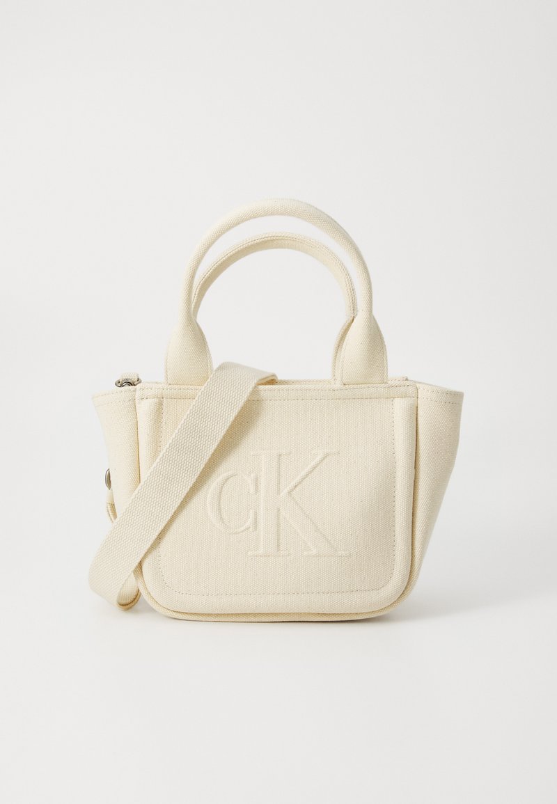 Cream fabric handbag with dual top handles and a removable shoulder strap. Features embossed "CK" logo on front and structured shape.