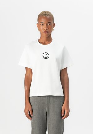 White cotton t-shirt featuring a black smiley face graphic at the center, short sleeves, a round neckline, and a relaxed fit.