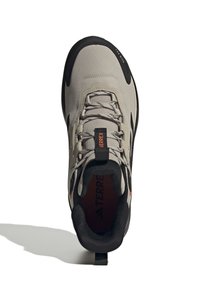 Chaussure de randonnée gris clair avec une tige texturée, des accents noirs et une pointe renforcée. Comprend une languette et un branding orange contrastant.