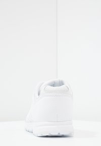 Vit sneaker med en slät läderliknande ovandel, texturerade accenter, vadderad krage och gummisula med ett mönster.