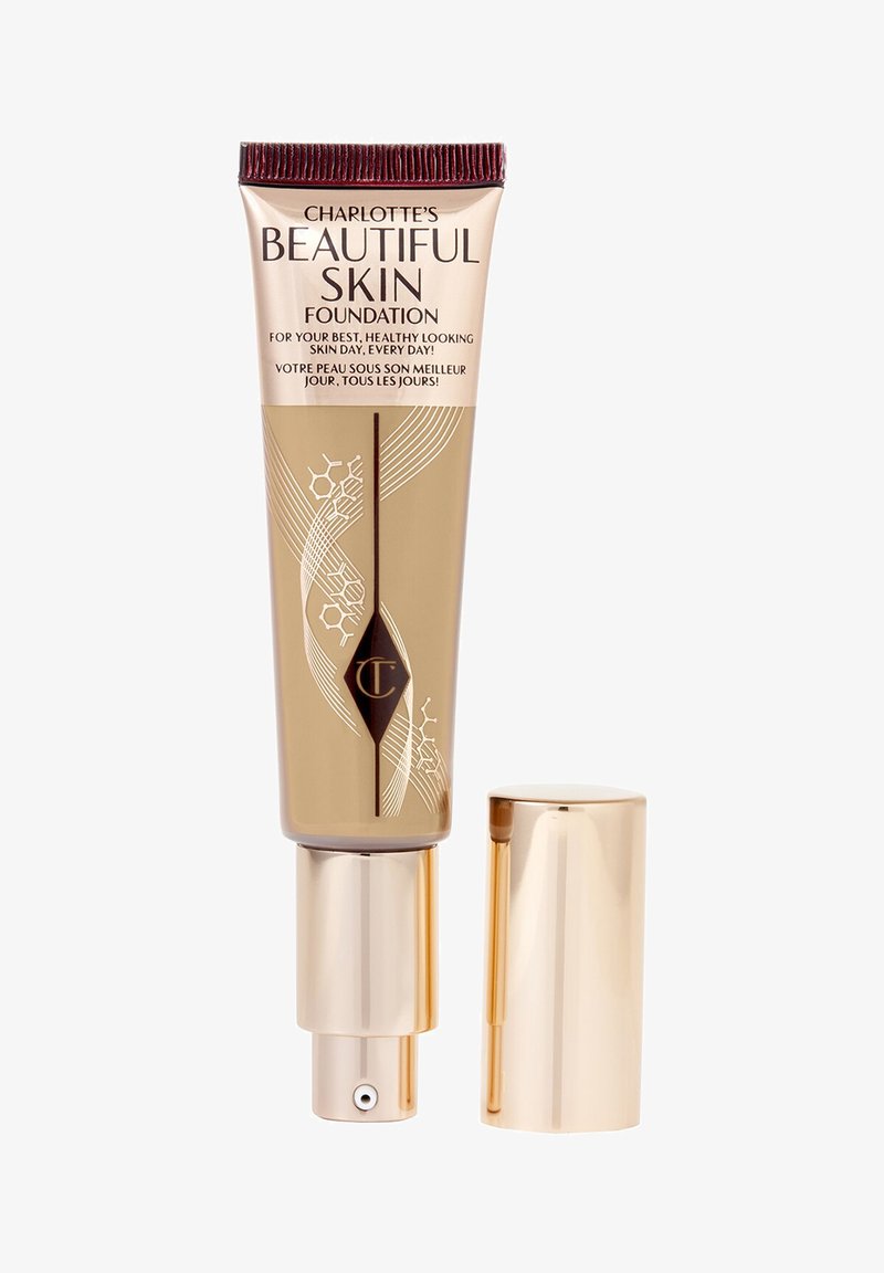 Charlotte’s Beautiful Skin Foundation tube with gold pump and cap, beige and rose gold packaging with decorative white lines and logo.