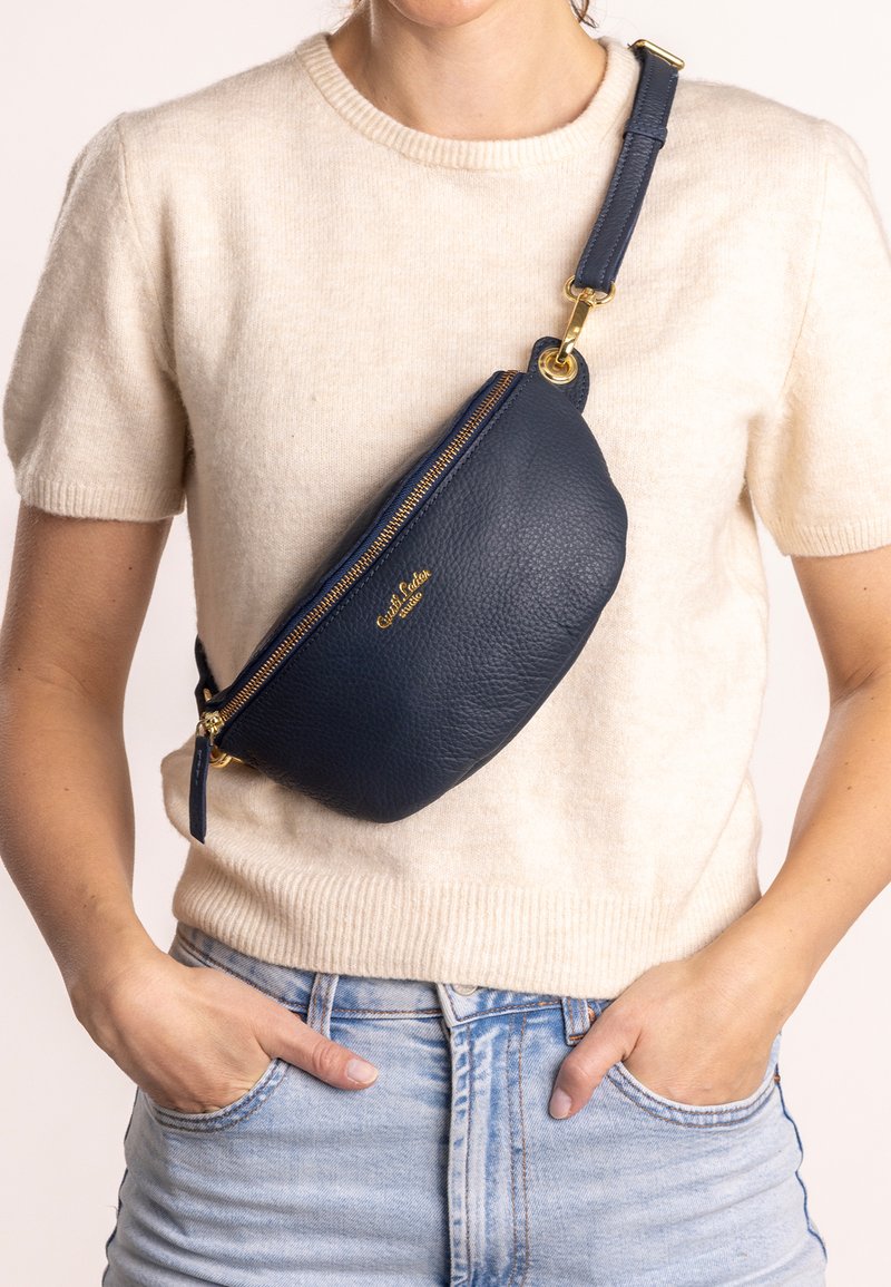 Borsa a tracolla in pelle blu marina con superficie strutturata, cerniera dorata e tracolla regolabile. Design compatto e curvo, posizionata in vita.