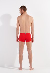 Shorts de bain rouges en matériau extensible, avec un design ajusté, une longueur courte et une étiquette de taille contrastante.