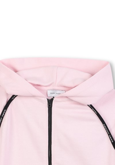 Lichtroze hoodie met een ritssluiting aan de voorkant, zwarte ritssluiting en een kap. Inclusief een label met de tekst "MARC JACOBS." Zachte stoftextuur.