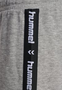 Grå sweatpants med en svart sidstripa med "hummel" och pilar i vitt. Mjuk tyg med en avslappnad passform.