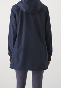 Marinblå vattentät jacka med huva, med elastiska ärmmuddar och en lös passform, parat med ljuslila träningsleggings.