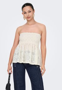 Weißes trägerloses Peplum-Top mit floralem Lochmuster und strukturiertem Oberteil, kombiniert mit dunkelblauen, weiten Jeans.